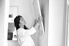 A young woman hangs up a picture in her new home.